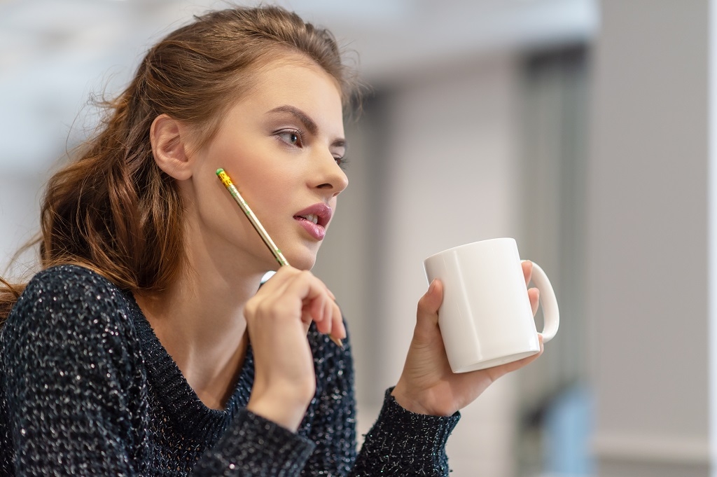 Thoughtful young woman making notes using notepad in kitchen. Ideas for business
